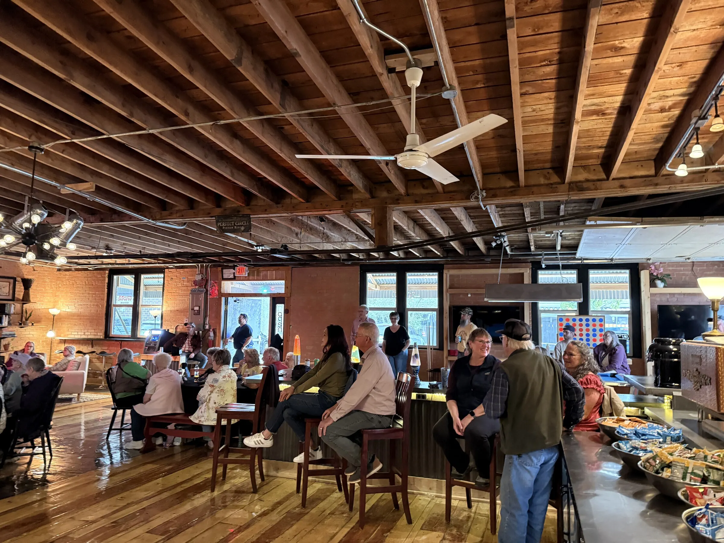Guests at tables and the bar in the open brick-and-timber room, string lights overhead