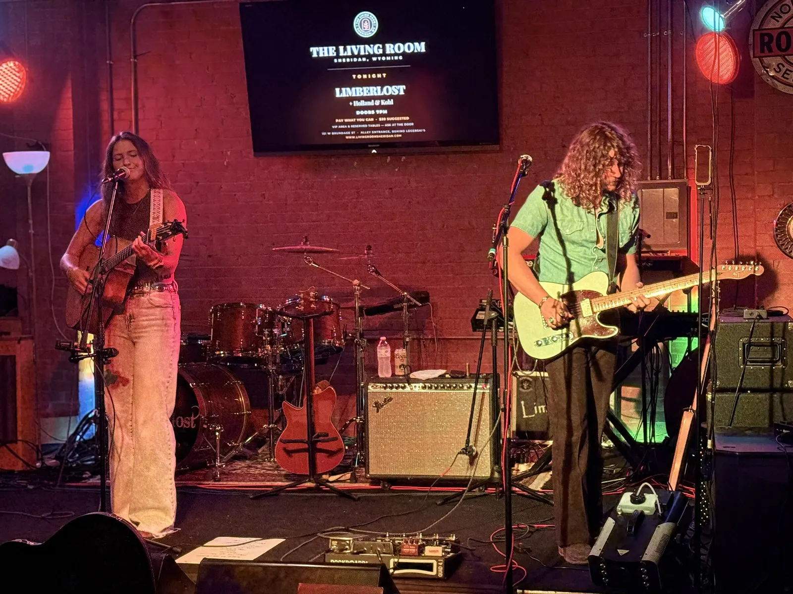 Two musicians on stage with the venue screen behind them